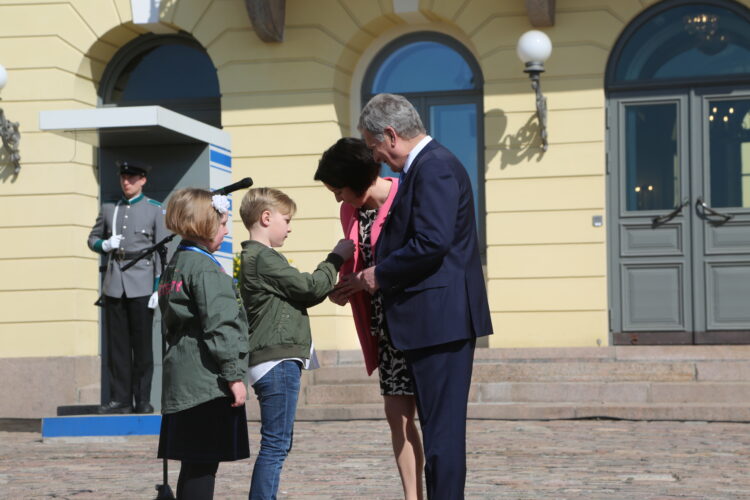 Vappukukka myyty. William Koivusalo kiinnittää keräysmerkin rouva Haukion takkiin. Kuva: Riikka Hietajärvi/Tasavallan presidentin kanslia