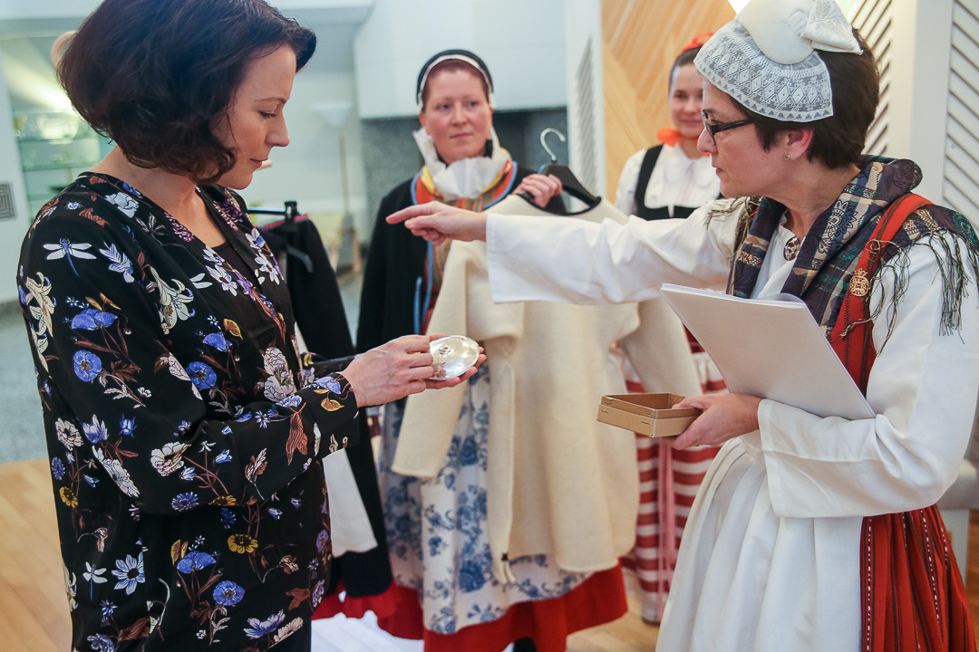 Taina Kangas esittelee puvun hopeista paljinsolkea, joka sulkee paidan etuhalkion. Kuva: Matti Porre/Tasavallan presidentin kanslia