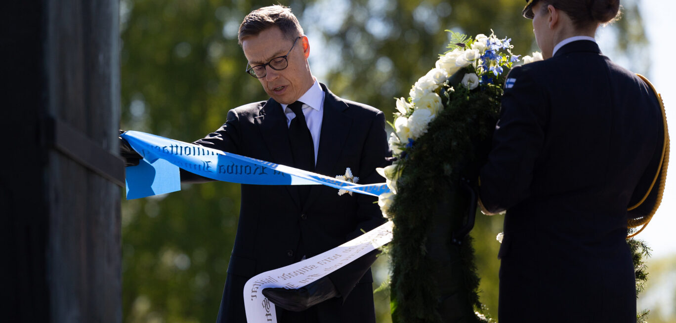 Republikens president Alexander Stubb läser texten på banden av en krans vid Hjältekorset på Sandudds begravningsplats.