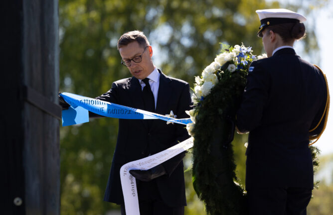 Republikens president Alexander Stubb läser texten på banden av en krans vid Hjältekorset på Sandudds begravningsplats.