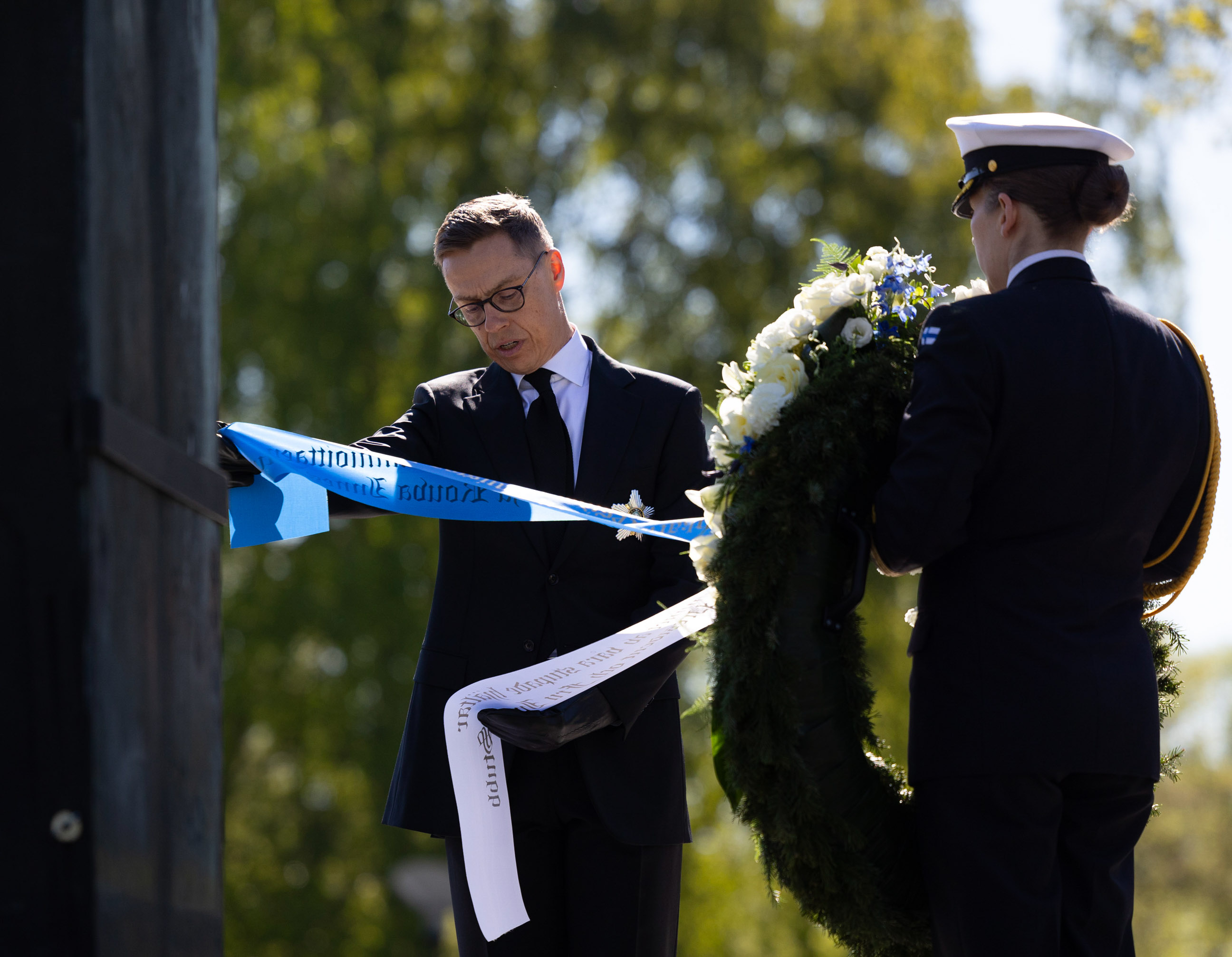 Republikens president Alexander Stubb läser texten på banden av en krans vid Hjältekorset på Sandudds begravningsplats.